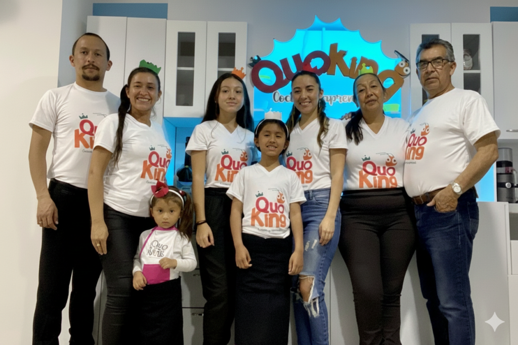 Equipo completo de Quoking, incluyendo niños y adultos, posando en la cocina con camisetas blancas con el logo Quoking. Foto horizontal de la familia y educadores para blog.